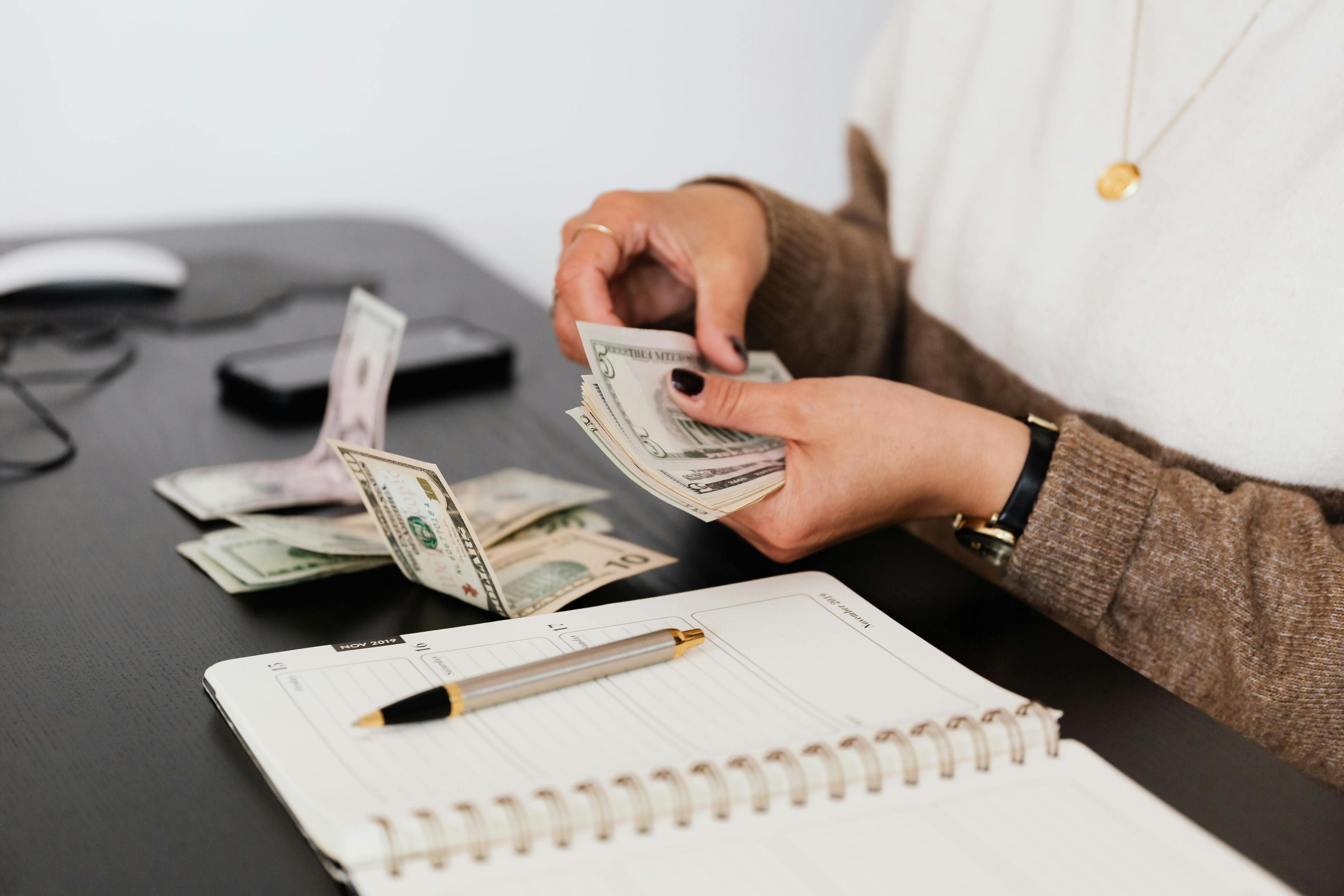 A woman counts money and types on a calculator, figuring out her budget.
